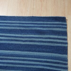 Navy and light blue striped flatweave rug shown on light blonde hardwood flooring.