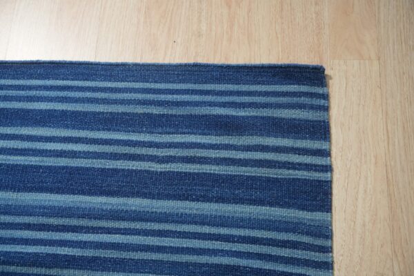 Navy and light blue striped flatweave rug shown on light blonde hardwood flooring.