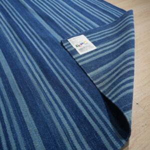 Two-tone blue striped rug showing the backing and product tag on light wood flooring.