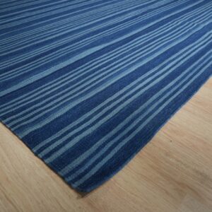Deep blue and light blue striped flatweave rug displayed on light blonde wood flooring.