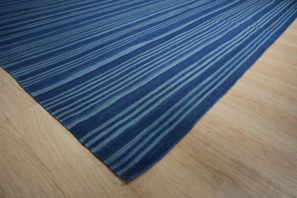 Deep blue and light blue striped flatweave rug displayed on light blonde wood flooring.