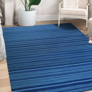 A blue and teal striped rug lies on wood floors next to a white armchair and a potted plant.