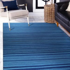 A blue striped rug lies on white tile floor beneath a cream armchair and black sofa.