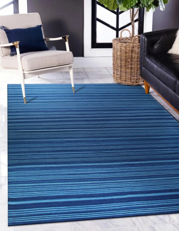 A blue striped rug lies on white tile floor beneath a cream armchair and black sofa.