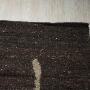 Dark brown textured rug with a light vertical stripe rests on light wood plank flooring.