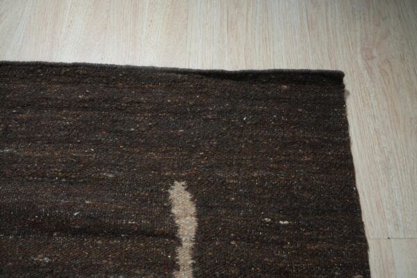 Dark brown textured rug with a light vertical stripe rests on light wood plank flooring.