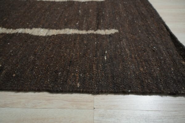 Dark brown speckled rug featuring tan horizontal stripes on light plank wood flooring.