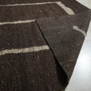 A textured dark brown rug featuring light beige stripes is displayed on pale plank flooring.