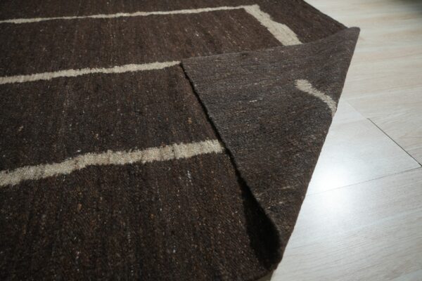 A textured dark brown rug featuring light beige stripes is displayed on pale plank flooring.
