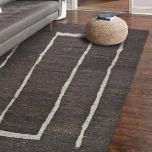 Charcoal rug with thick white angled lines, placed on wood floors next to a gray sofa and pouf.