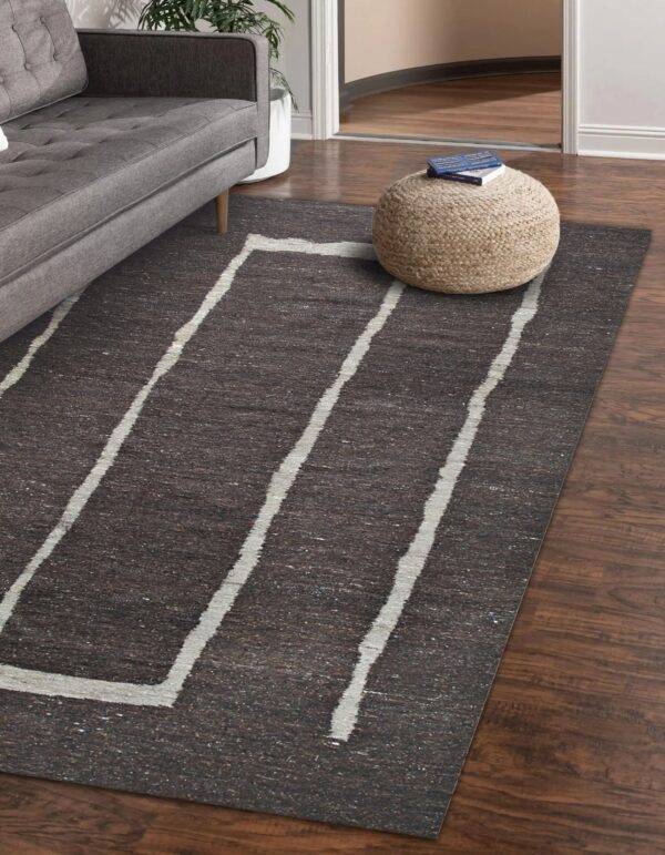 Charcoal rug with thick white angled lines, placed on wood floors next to a gray sofa and pouf.