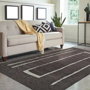 Dark brown rug with thick white geometric stripes on a gray floor beneath a light beige sofa.