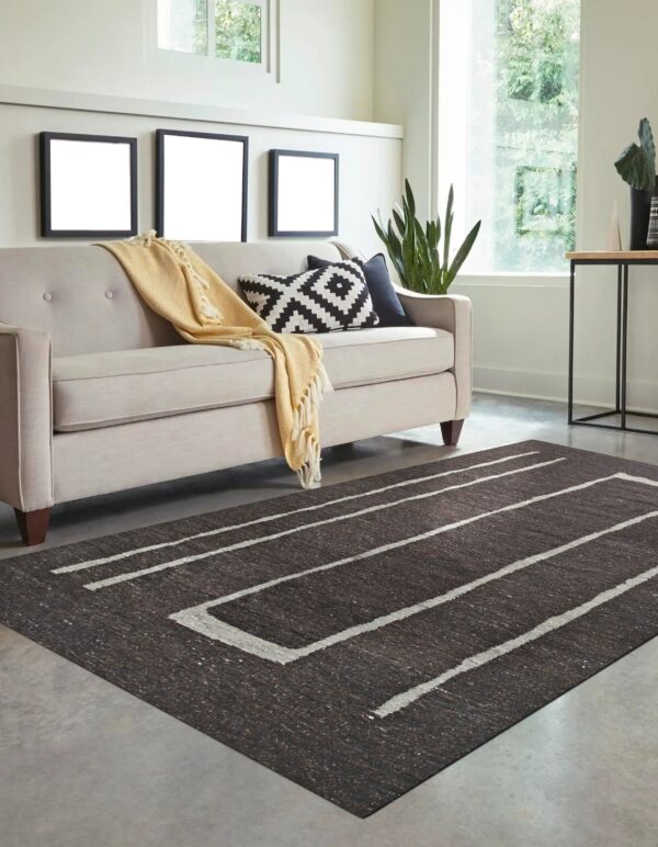 Dark brown rug with thick white geometric stripes on a gray floor beneath a light beige sofa.