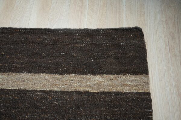 Coarse brown and beige striped rug lying on light plank wood flooring.