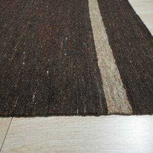 Dark brown speckled rug with a natural tan vertical stripe over light wood floorboards.