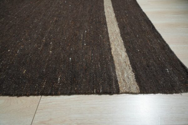Dark brown speckled rug with a natural tan vertical stripe over light wood floorboards.