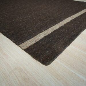 Dark brown speckled rug with a beige stripe sits diagonally on light wood plank flooring.