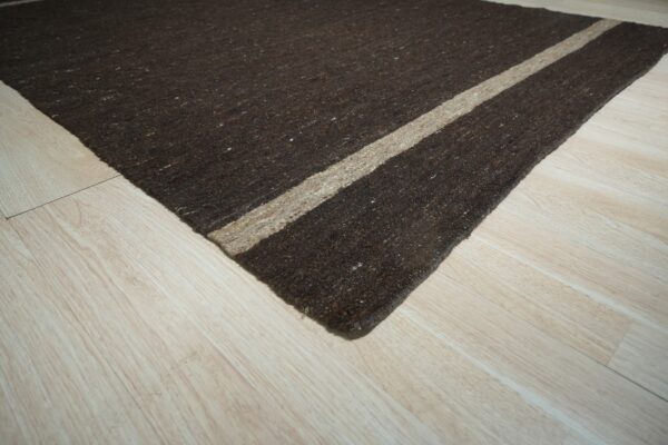 Dark brown speckled rug with a beige stripe sits diagonally on light wood plank flooring.