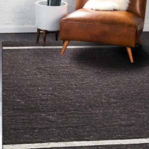 Speckled dark brown area rug with a thick white border stripe under a leather chair and potted plant.