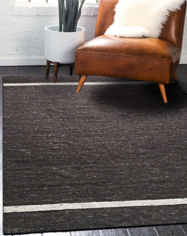 Speckled dark brown area rug with a thick white border stripe under a leather chair and potted plant.