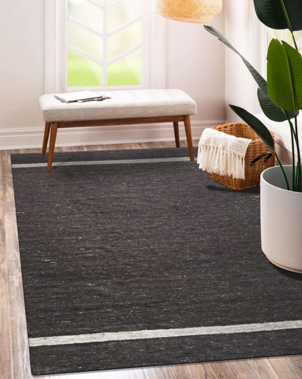 Speckled dark brown rug with thin gray stripes sits on wood flooring next to a bench and houseplant.