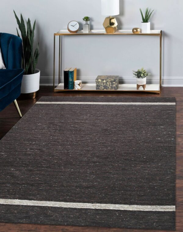 Charcoal textured area rug with thin beige stripes is centered beneath a gold console table.
