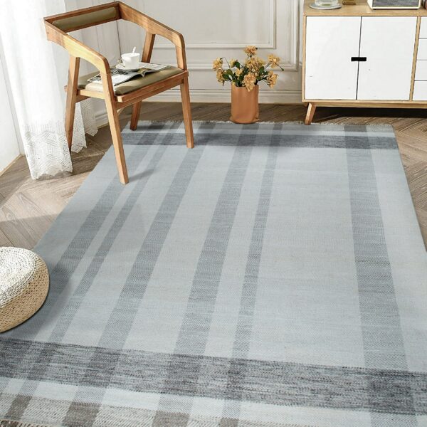 A flatwoven gray and blue striped rug with a visible chevron weave sits on herringbone wood flooring.