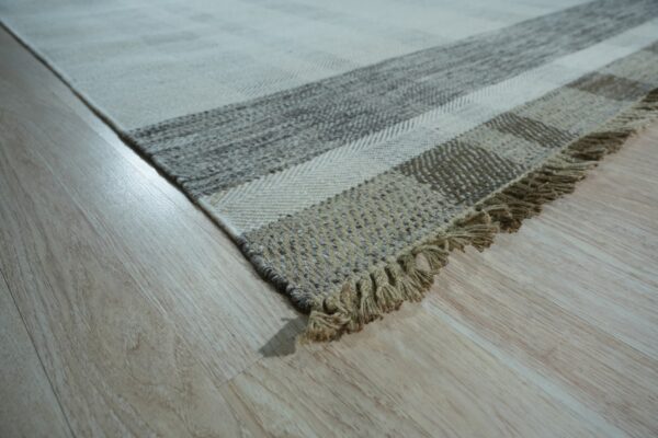Low-angle view of a striped flatweave rug in cream and natural tones with fringe on light wood.