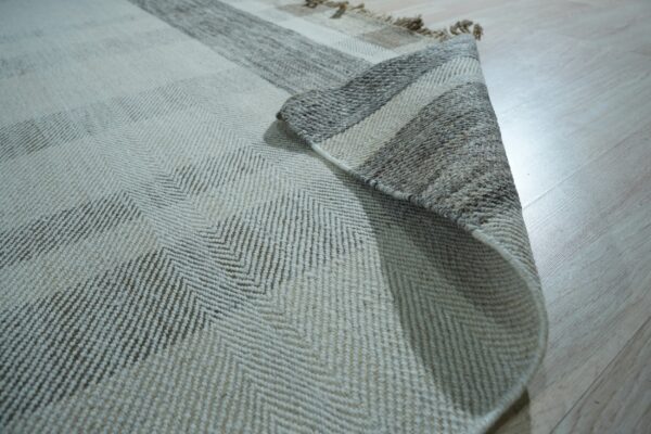 Cream and brown chevron rug partially rolled, showing striped backing on a light wood floor.