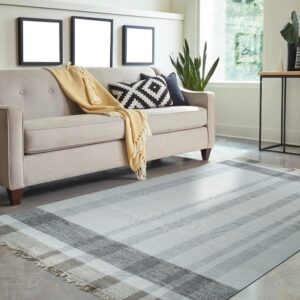 Gray and white plaid flatweave rug on concrete flooring beneath a neutral sofa.