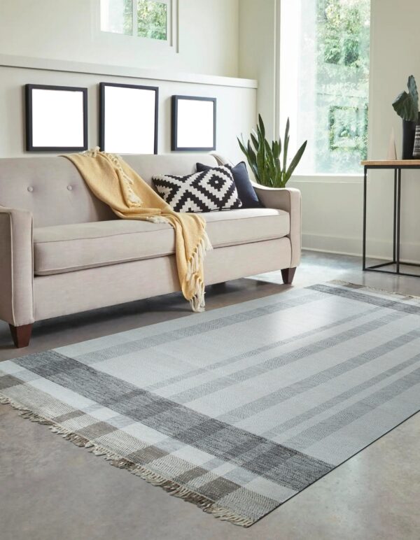Gray and white plaid flatweave rug on concrete flooring beneath a neutral sofa.