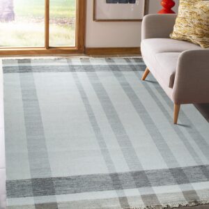 Chevron-textured flatweave rug in light and dark gray stripes positioned beneath a beige sofa by a window.