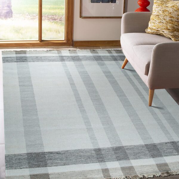 Chevron-textured flatweave rug in light and dark gray stripes positioned beneath a beige sofa by a window.