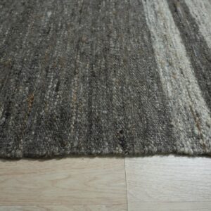 Textured striped rug featuring mottled charcoal and light gray colors on pale wooden flooring.