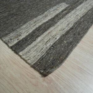 A textured rug with mixed dark gray and light beige stripes rests on pale wood flooring.