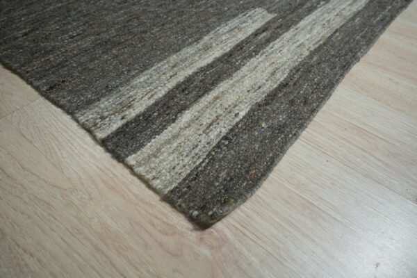 A textured rug with mixed dark gray and light beige stripes rests on pale wood flooring.
