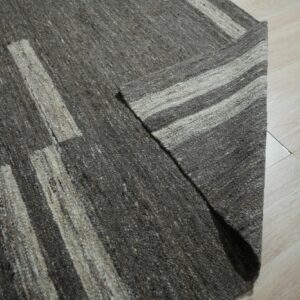 A chunky heathered gray rug with light vertical stripes partially rests on pale blonde wood plank flooring.