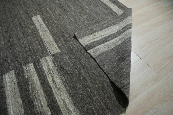 A nubby, heathered dark gray rug with light vertical striping rests partially folded on pale wood flooring.