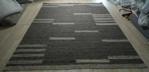 Flatwoven gray and tan rug featuring an abstract striped geometric design on light wood floors.