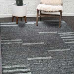 Textured gray rug with abstract light gray stripes on dark flooring beside a chair and white brick wall.
