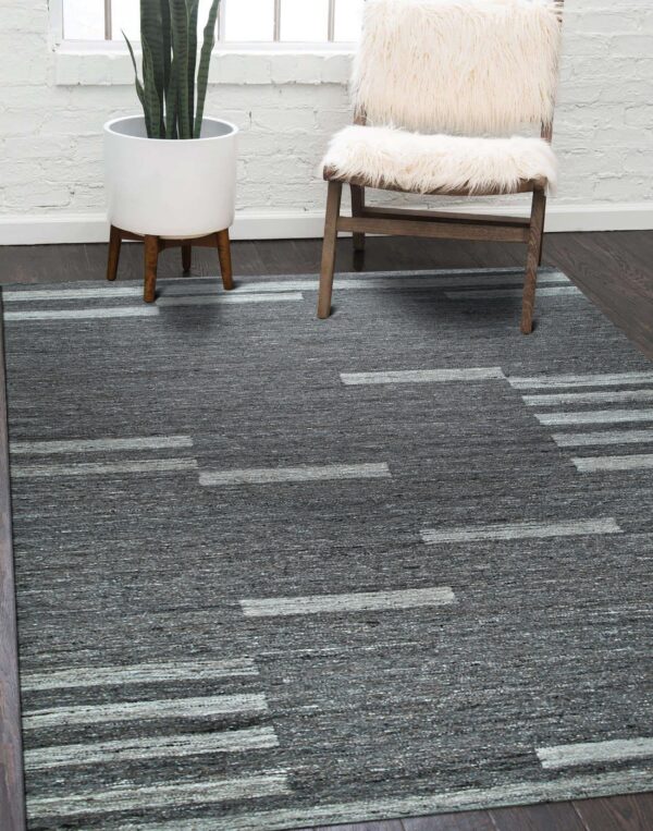 Textured gray rug with abstract light gray stripes on dark flooring beside a chair and white brick wall.