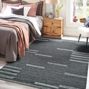 Dark gray heathered rug with light geometric stripe patterns anchors a cozy bedroom setting on wood floors.
