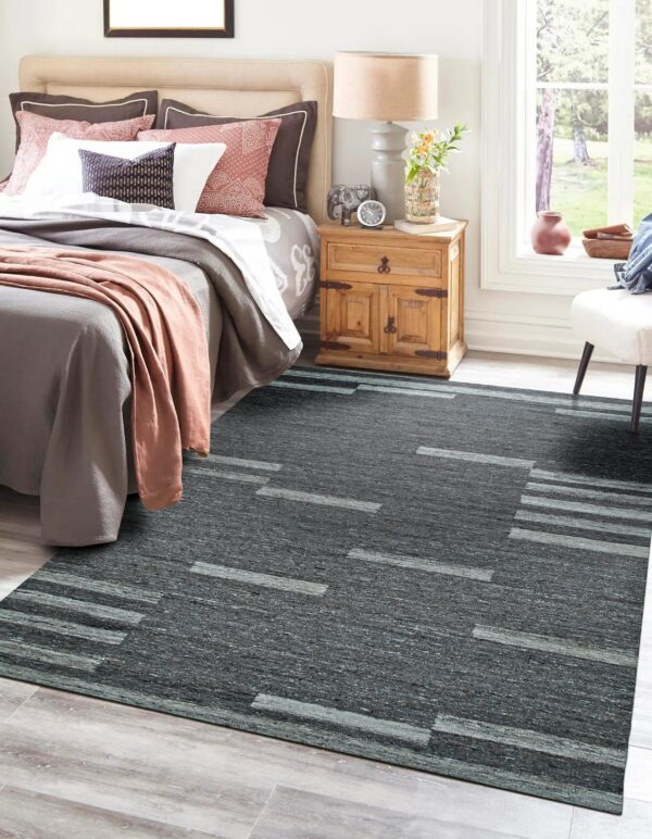 Dark gray heathered rug with light geometric stripe patterns anchors a cozy bedroom setting on wood floors.