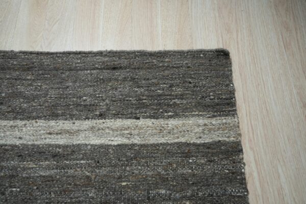 Flatweave rug corner with thick gray and light beige horizontal stripes on light wood planks.
