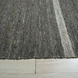 Mottled dark gray low-pile rug with a broad cream vertical stripe rests on bleached wood planks.