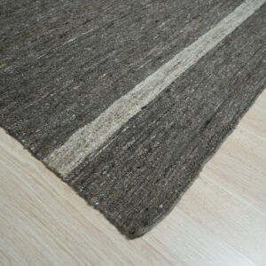 Diagonal view of a textured charcoal and beige striped rug lying on light wood laminate.