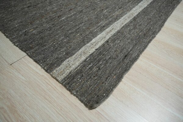 Diagonal view of a textured charcoal and beige striped rug lying on light wood laminate.
