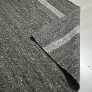 A gray nubby textured rug with tan flecks and white stripes rests on pale blonde wood flooring.