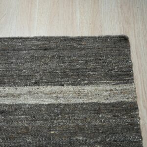Textured, striped rug in dark gray and off-white rests on vertical light wood plank flooring.