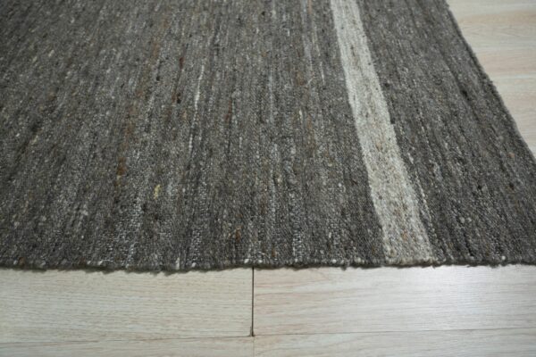 Textured gray and brown speckled rug with wide off-white stripes rests on light blonde wood flooring.